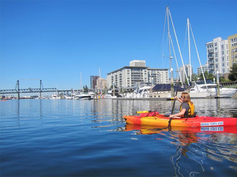 A woman in a red kayak paddling towards the Murray Morgan Bridge.